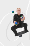 junger Mann jongliert mit Baellen und balanciert auf einem Rola Bola Balancier- Brett, young man juggling with balls and balancing on a rola bola balance board