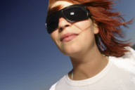 Portraet einer jungen rothaarigen Frau mit Sonnenbrille im Wind, portrait of a redhaired woman with sun glasses in the wind