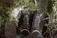 Woman standing on a Tree Stub looking down to her Boots