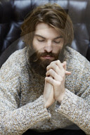 Young Man wearing a wool Pullover and sitting on an Armchair