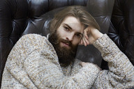 Young Man wearing a wool Pullover and sitting on an Armchair