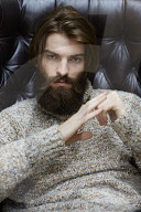 Young Man wearing a wool Pullover and sitting on an Armchair