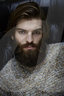 Young Man wearing a wool Pullover and sitting on an Armchair