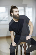 Young Man wearing a black T-Shirt and sitting on a Stool