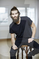 Young Man wearing a black T-Shirt and sitting on a Stool