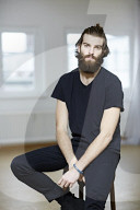 Young Man wearing a black T-Shirt and sitting on a Stool