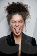 Woman with curly Hair wearing a Blazer sticking Tongue out