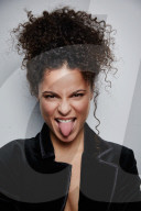 Woman with curly Hair wearing a Blazer sticking Tongue out