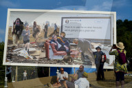 Festival-goers sit under an anti-Brexit billboard, a collaboration by Cold War Steve and Led By Donkeys.