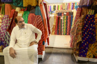 Shopkeeper seated outside his shop surrounded by  colourful material, Souq Waqif, Doha, Qatar, Middle East