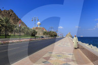 Man wearing dishdasha walks along Mutrah Corniche with national flags, flower beds and Giant Incense Burner, Muscat, Oman