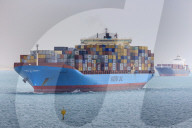 Convoy of container ships transiting the Suez Canal loom through air thick with desert sand, Great Bitter Lake, Ismalia, Egypt