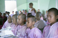 Buddhist novice schoolgirls conducting class meditation in the school classroom before lessons, teacher in background