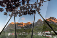 Midnight sun on dried fish framed by fishing village and peaks, Reine, Nordland county, Lofoten Islands, Arctic, Northern Norway, Scandinavia, Europe