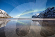 Northern lights and stars light up the sandy beach framed by snowy peaks Ersfjord Senja Troms County Norway Europe