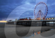 Big wheel  and amusements on Central Pier at sunset with young women looking on, Blackpool, Lanscashire, Northern England.