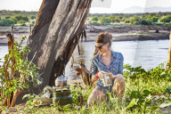 A young woman boil some water for coffee in the early morning light while camping in Samburu National Park, Kenya