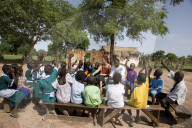Volunteer Pimary Cluster Teacher trainer, Fiona Stevenson leading story time and singing in the yard of primary school  in Fori,  the unqualified teacher who she has been training on her left is Alpha Ajallow.  The Gambia.