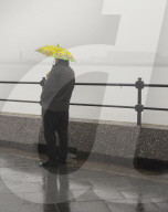A man waits in the rain under a childs umbrella