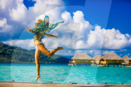 Girl jumping in front of overwater bungalows, Le Taha'a Resort, Tahiti, French Polynesia