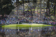 Spectators fill the hill behind the 9th green of the Par 3 course as players finish their round at Augusta National Golf Club.