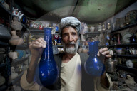 A glass blower holds up blue glass goards in a trinket shop in Herat in Afghanistan