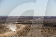 A car leaves a cloud of dust as it apporachs along the long dusty road from the Fish River Canyon, Namibia, Africa