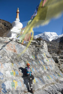 A woman trekking in the Langtang valley in Nepal stops near a colorful Mani Stone wall below a Stupa decorated with prayer flags