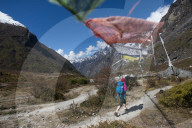 In the Langtang valley in Nepal a woman treks under a string of prayer flags path between Langtang village and Kyanjin Gompa