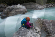 A woman takes a break from the trail and sits beside the Langtang Khola near the little village of Riverside on a misty evening
