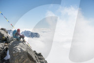 A woman sits under prayer flags marking the top of the Laurebina La which is the pass between the Langtang region and Helmabu in