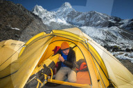 A mountaineer in Nepal packs his bag in preparation to climb Ama Dablam, the 6,856m peak in the distance