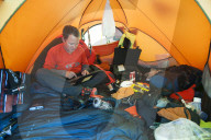 An Everest expeditioner sits among his mountain of equipment while he checks his email with a satelite modem