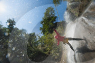 A man pauses to hold his arms in the falling water while canyoning in Nepal
