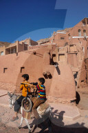 Boy with donkey gives bicyclist a lift in 1500 year old traditional village of red mud brick houses, Abyaneh, Iran