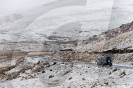 A four wheel drive vehicle negotiates a road through a wintry landscape in the Elan Valley area in Powys, Wales, UK.