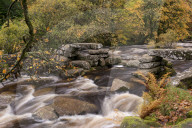River Dart tumbling past an ancient stone clapper bridge at Dartmeet, Dartmoor National Park, Devon, England. Autumn (October) 2015.