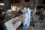 Smiling woman with thanaka paste on her face, folding sheets of pressed, cooked rice in rice noodle factory, Hsipaw, Shan state.