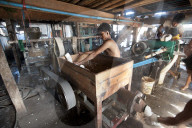 Men squeezing cooked rice through a machine before pressing into flat sheets to make fresh rice noodles, Hsipaw, Shan state.