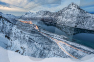 The snowy peaks above the frozen sea framed by the blue lights of dusk Gryllefjorden Senja Troms County Norway Europe