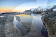 Orange sky at sunset reflected on snowy peaks and the frozen sea surrounded by rocks Tungeneset Senja Troms County Norway Europe