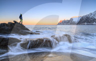 Hiker admires the waves of the icy sea crashing on the rocky cliffs at dawn Tungeneset Senja Troms county Norway Europe