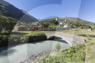 Typical red Swiss train on Hospental Viadukt surrounded by creek and green meadows, Andermatt, Canton of Uri, Switzerland, Europe