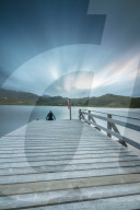 Hiker on wooden deck admires the sea illuminated by blue lights at night, Holdalsvatnet, Vestvagoy, Lofoten Islands, Norway, Scandinavia, Europe