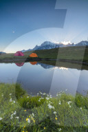Camping tents in the green meadows surrounded by flowers and alpine lake Mont De La Saxe Courmayeur Aosta Valley Italy Europe