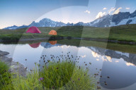 Camping tents in the green meadows surrounded by flowers and alpine lake Mont De La Saxe Courmayeur Aosta Valley Italy Europe
