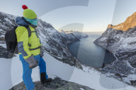 Hiker on top of the crest admires the village of Fjordgard framed by the frozen sea of the Ornfjorden Senja TromsÃ¸ Norway Europe