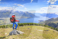 Hiker on green meadows admires Lake Como surrounded by woods Montemezzo Alpe Zocca Lombardy Italy Europe
