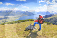 Hiker on green meadows admires Lake Como framed by snowy peaks Montemezzo Alpe Zocca Lombardy Italy Europe