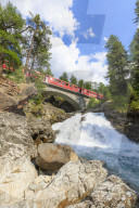 Bernina Express train surrounded by the alpine creek, Morteratsch, canton of GraubÃ¼nden, Engadin Valley, Switzerland, Europe